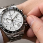 Srebrny zegarek Longines z chronografem na nadgarstku, ustawiany dłonią.