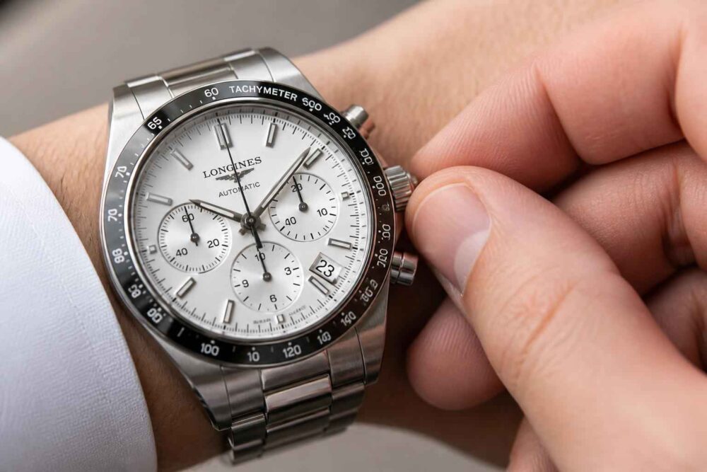 Srebrny zegarek Longines z chronografem na nadgarstku, ustawiany dłonią.